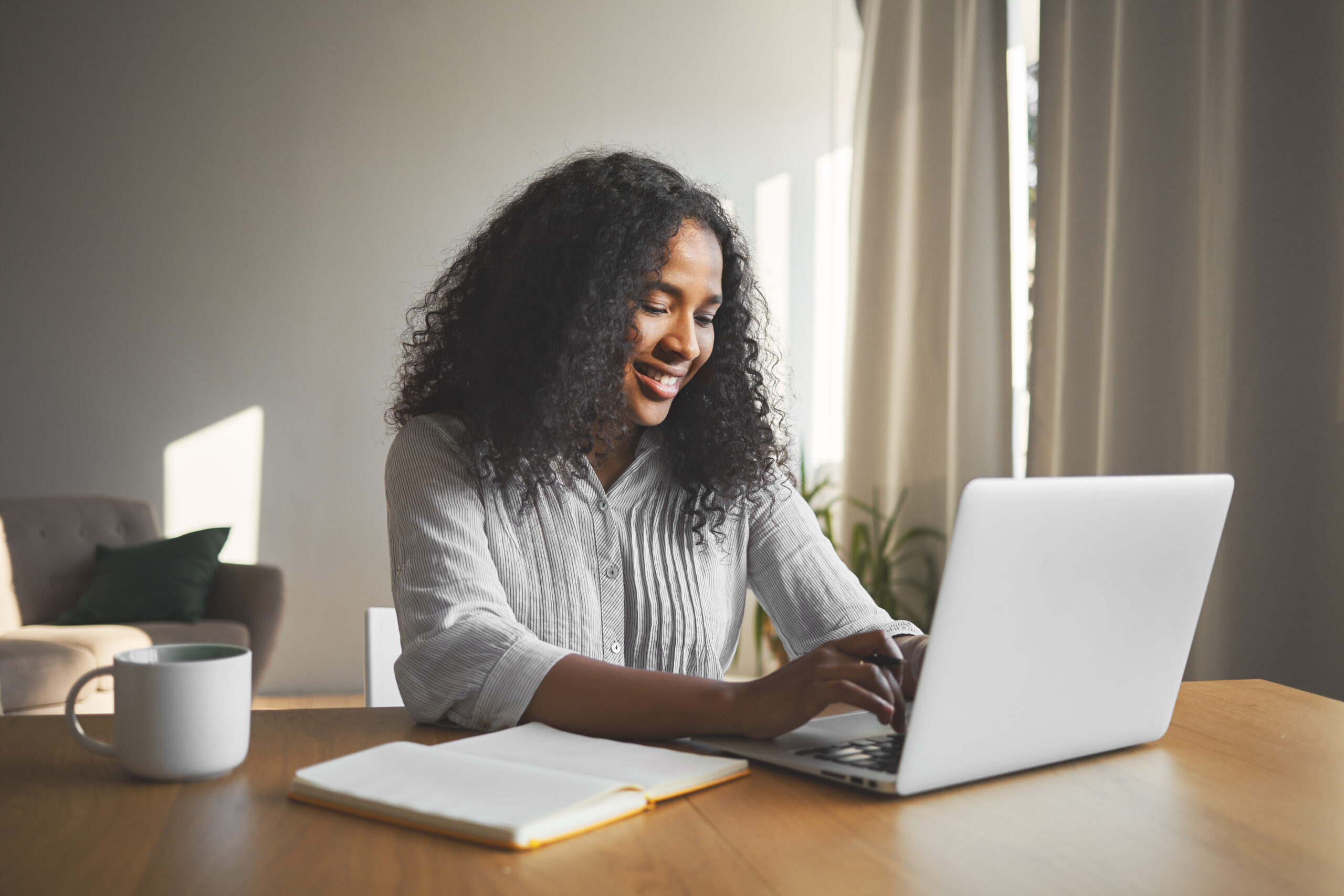 Gorgeous positive young dark skinned female blogger keyboarding